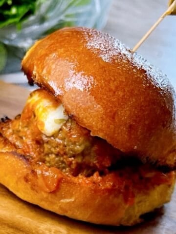 One meatball slider on a serving tray with melty cheese and sauce showing.