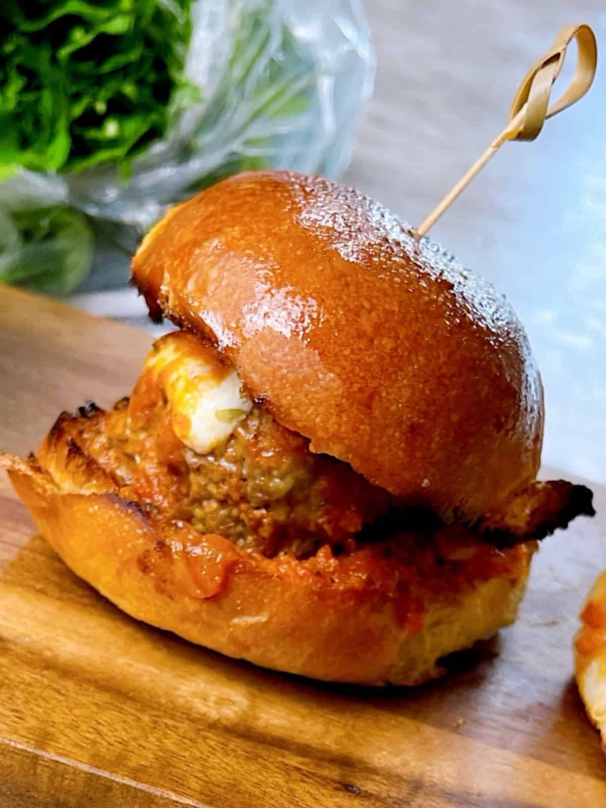 One meatball slider on a serving tray with melty cheese and sauce showing.