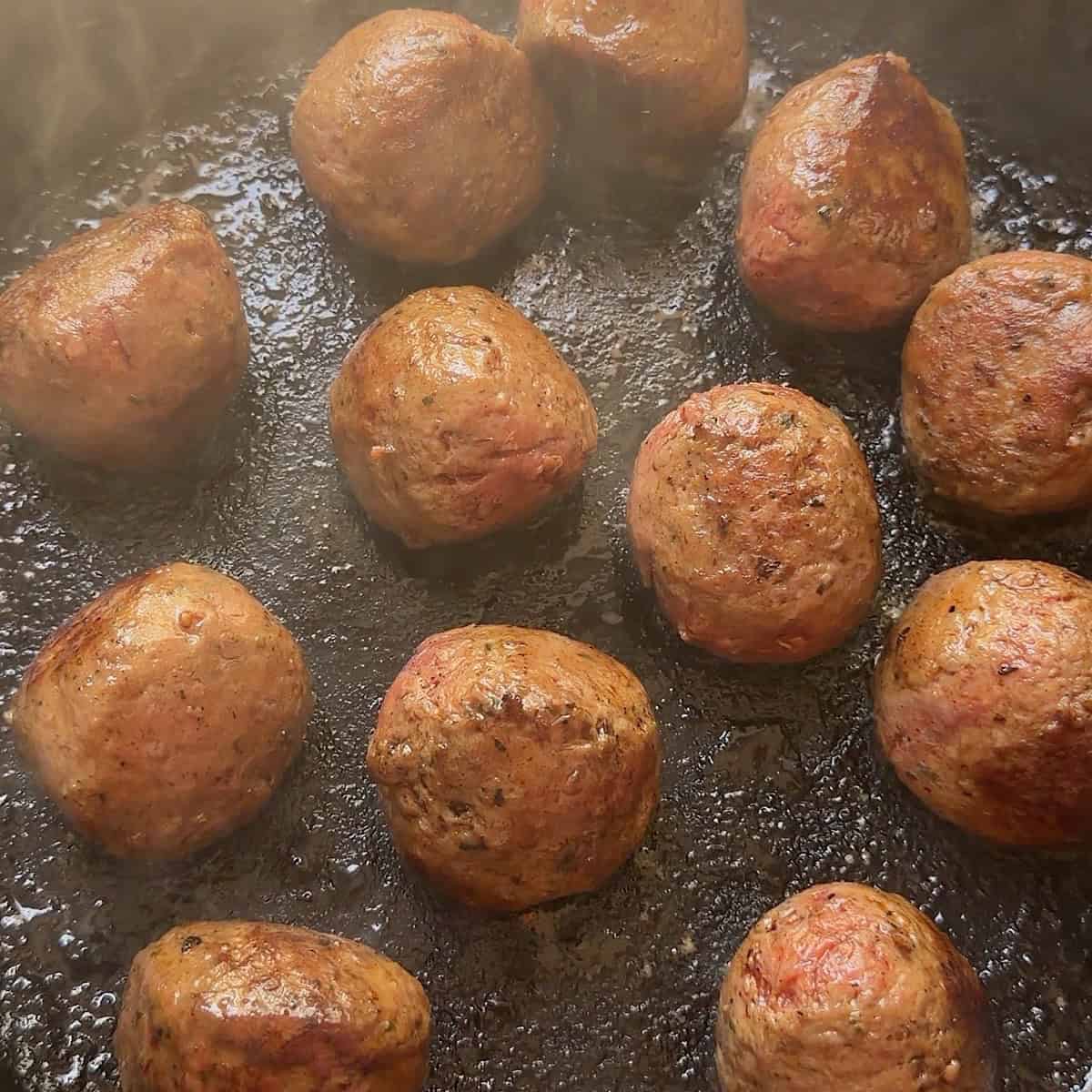 Meatballs browning in a skillet.