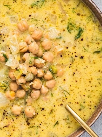 A bowl of Greek chickpea soup with lemon and a gold spoon.