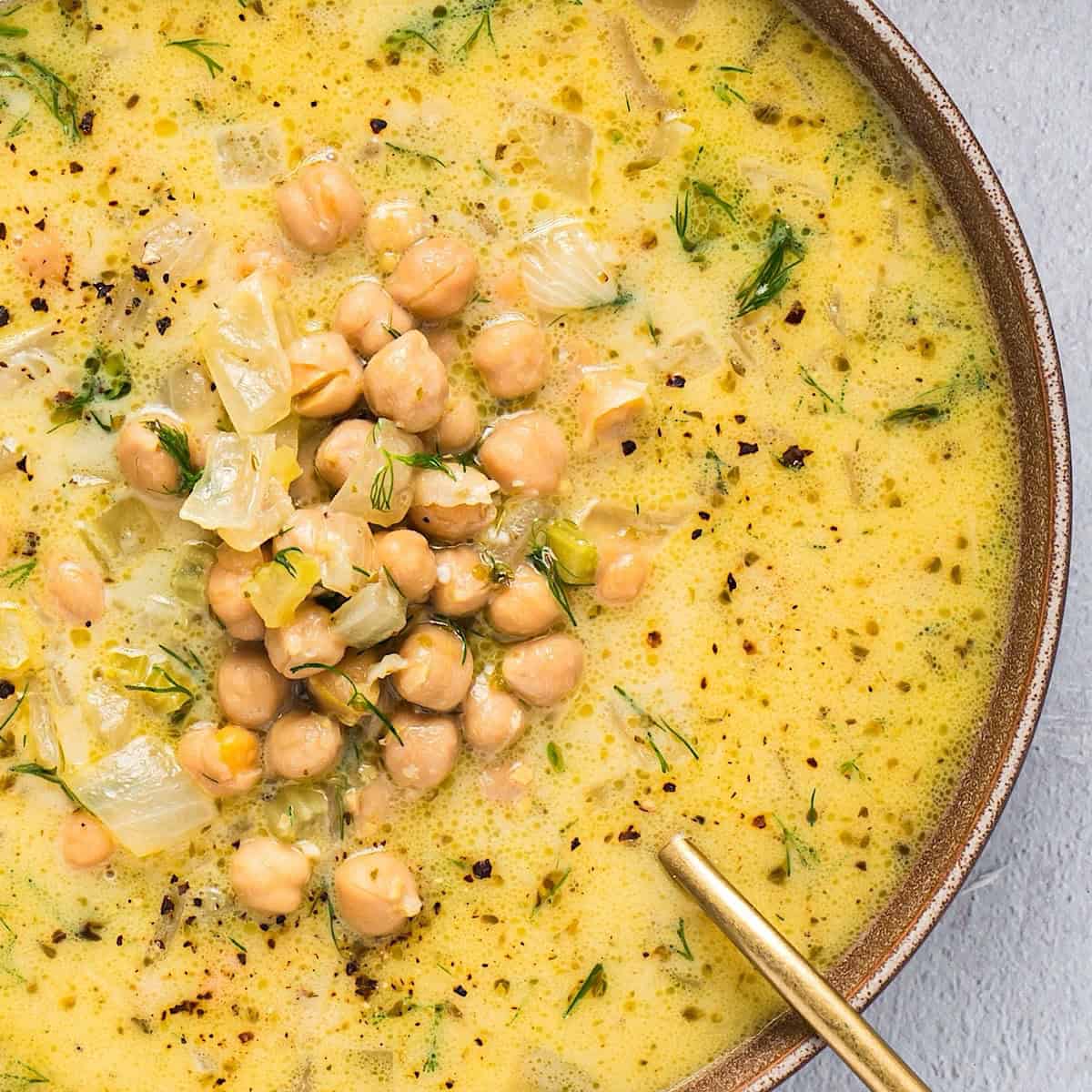 A bowl of Greek chickpea soup with lemon and a gold spoon.