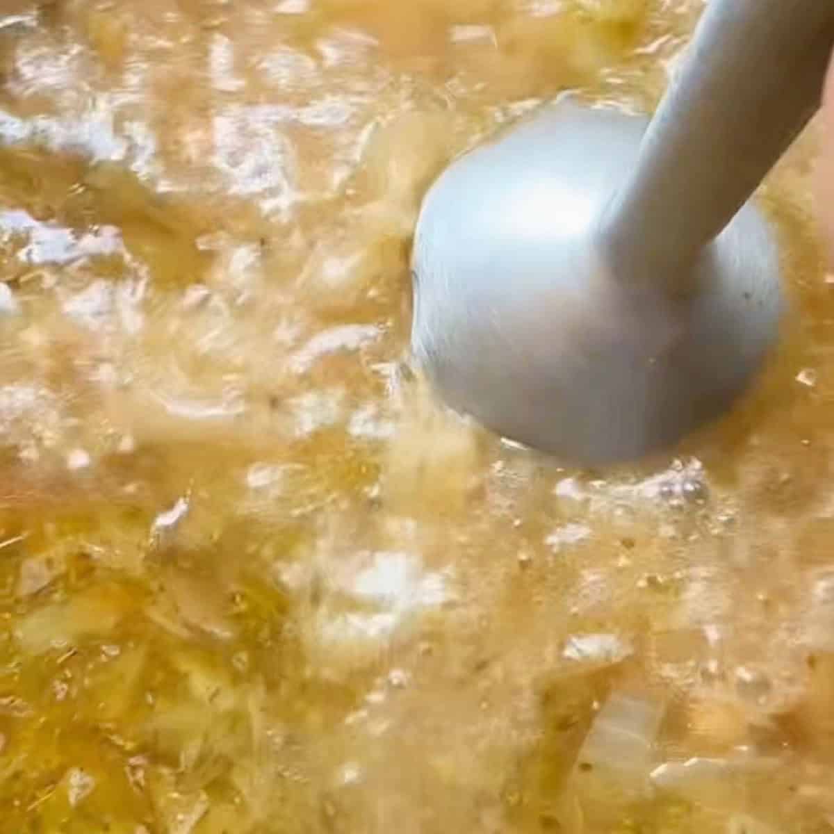 Using an immersion blender to blend part of the soup for a creamy texture.