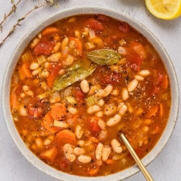 A wide bowl of Greek fasolada soup with gold spoon.