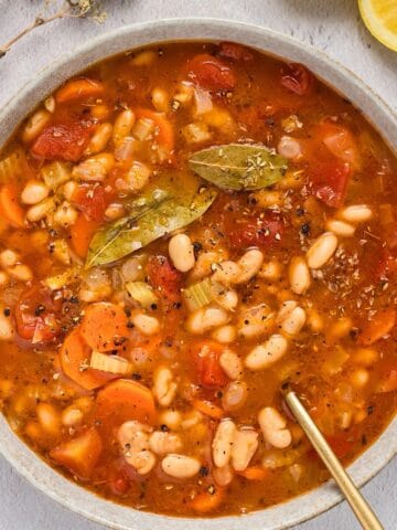 A wide bowl of Greek fasolada soup with gold spoon.