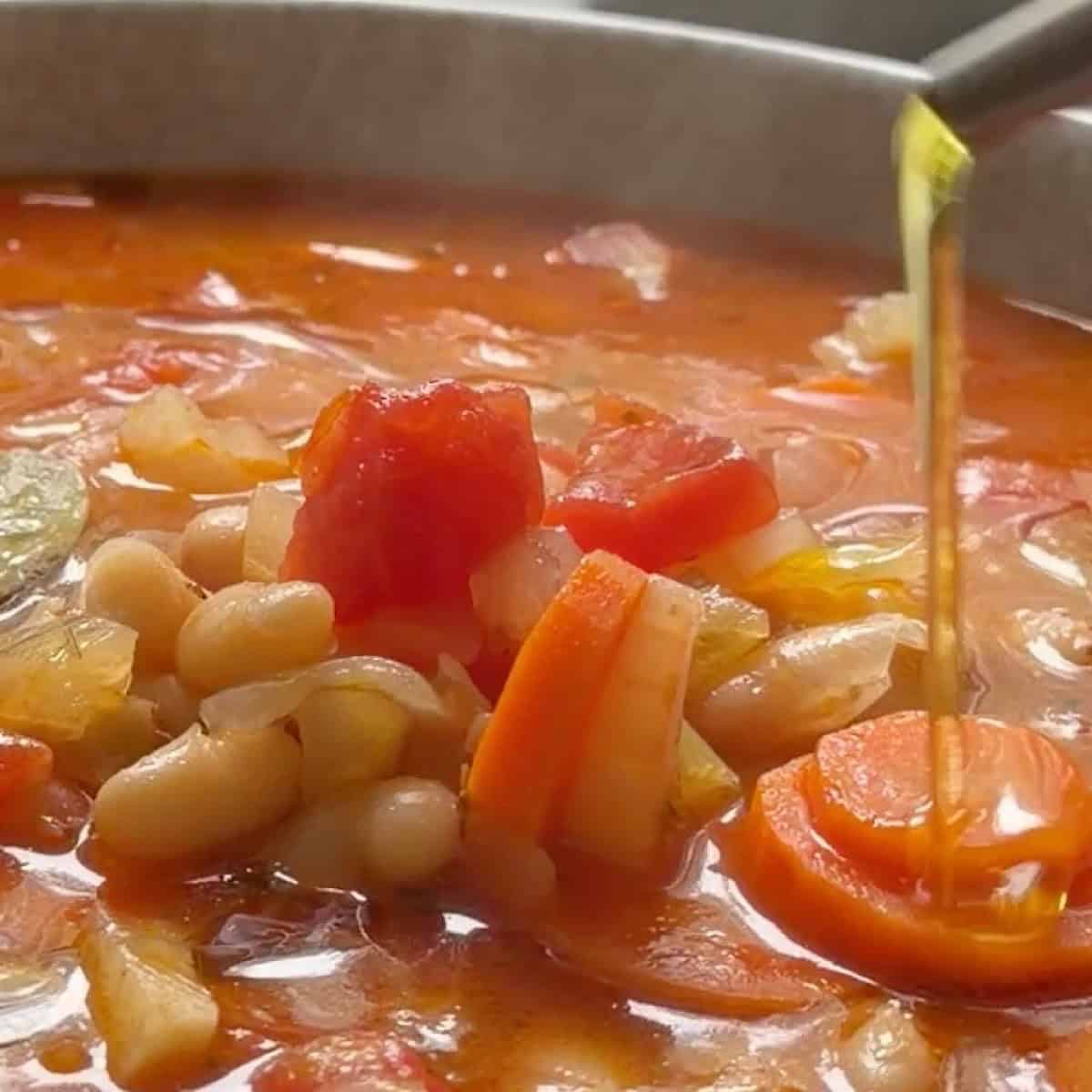 Drizzling olive oil over a bowl with fasolada soup ready to serve.
