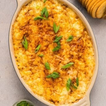Hot baked crab dip with cream cheese in a small ceramic dish plated near Ritz crackers and green onion.