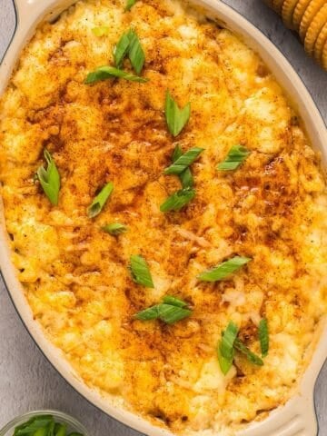 Hot baked crab dip with cream cheese in a small ceramic dish plated near Ritz crackers and green onion.