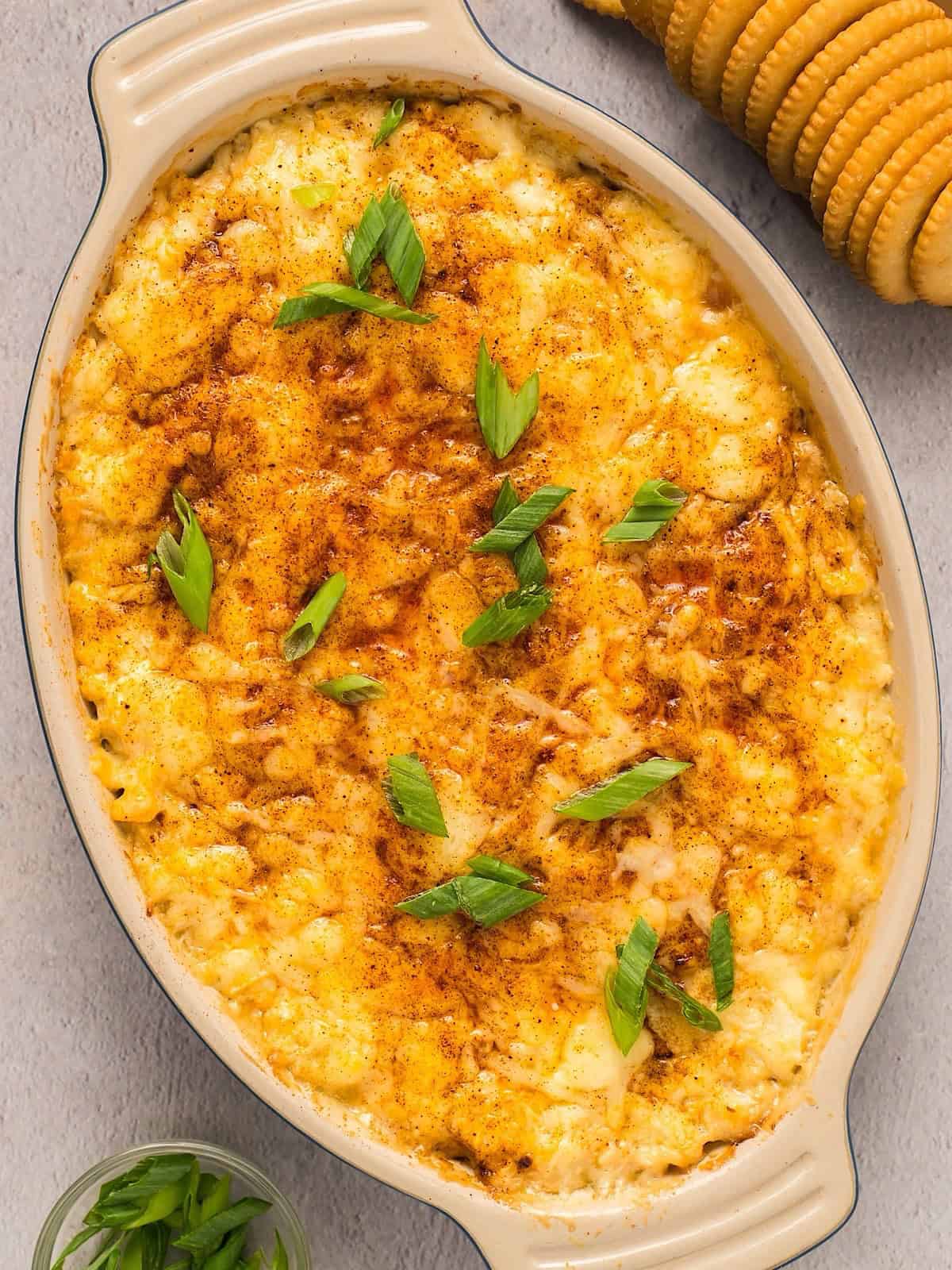 Hot baked crab dip with cream cheese in a small ceramic dish topped with paprika and green onion.