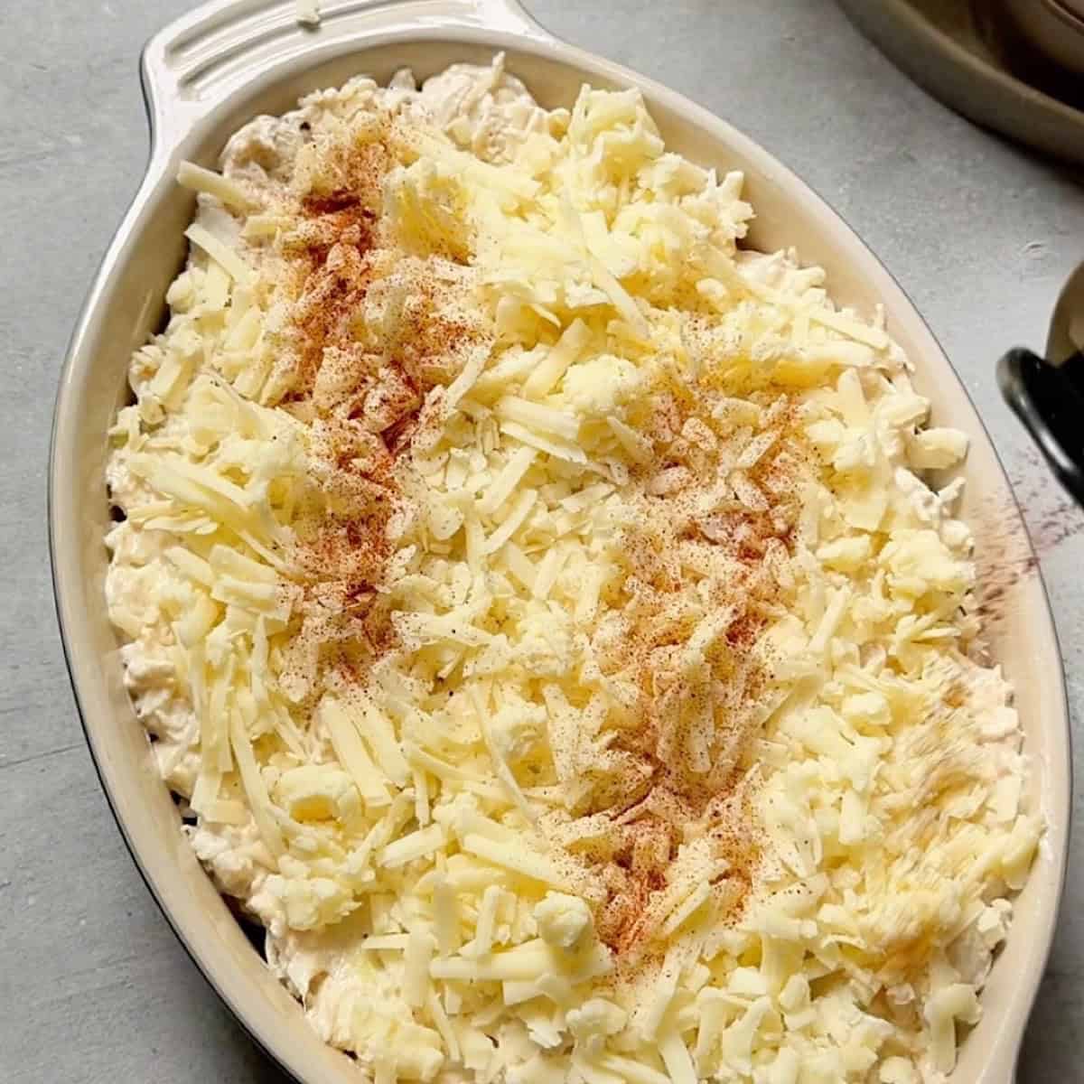 Crab dip arranged in a baking dish with white cheddar cheese and a dusting of paprika.