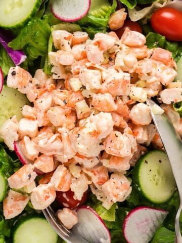 Old bay shrimp salad on a bed of greens and serving utensils.