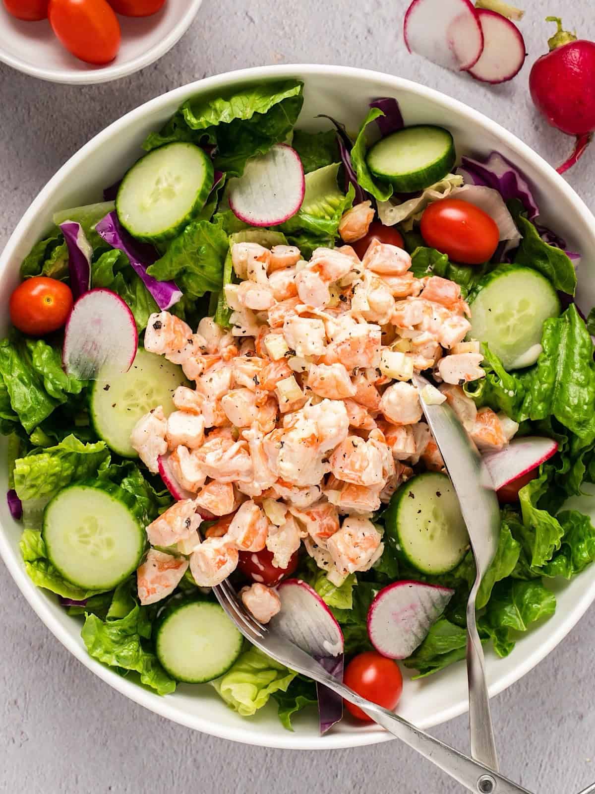 Old bay shrimp salad on a bed of greens in a white serving bowl.