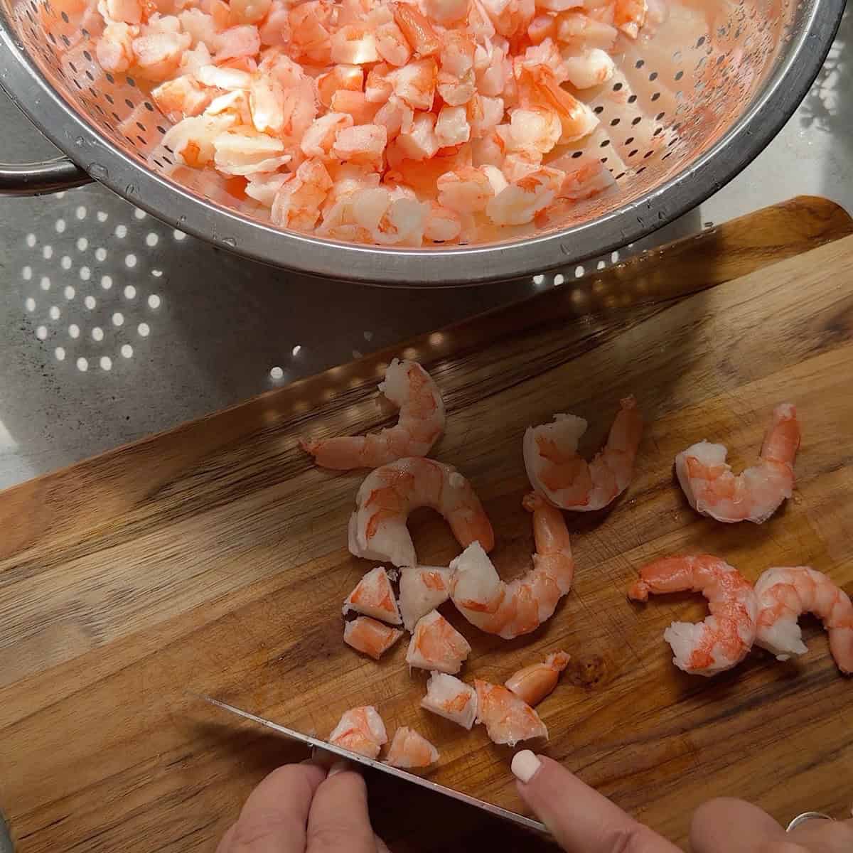 Chopping the shrimp on a cutting board near a colander.