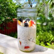 A mason jar of peaches and cream overnight oats with toppings sitting on a deck with sunshine highlighting ingredients.