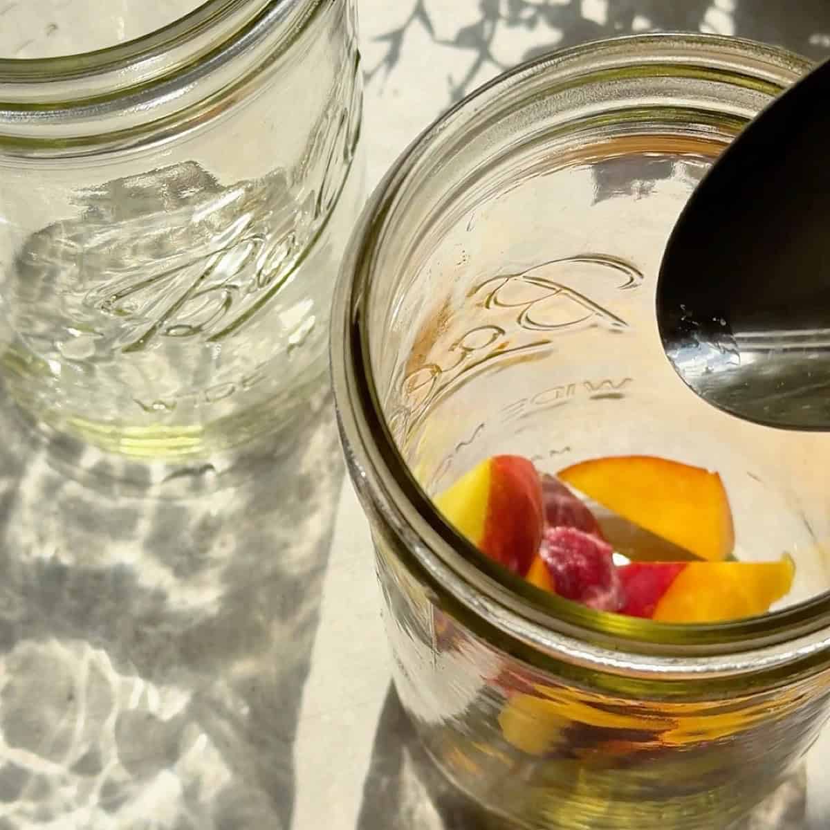Diced fresh peaches being added to the bottom of a mason jar.