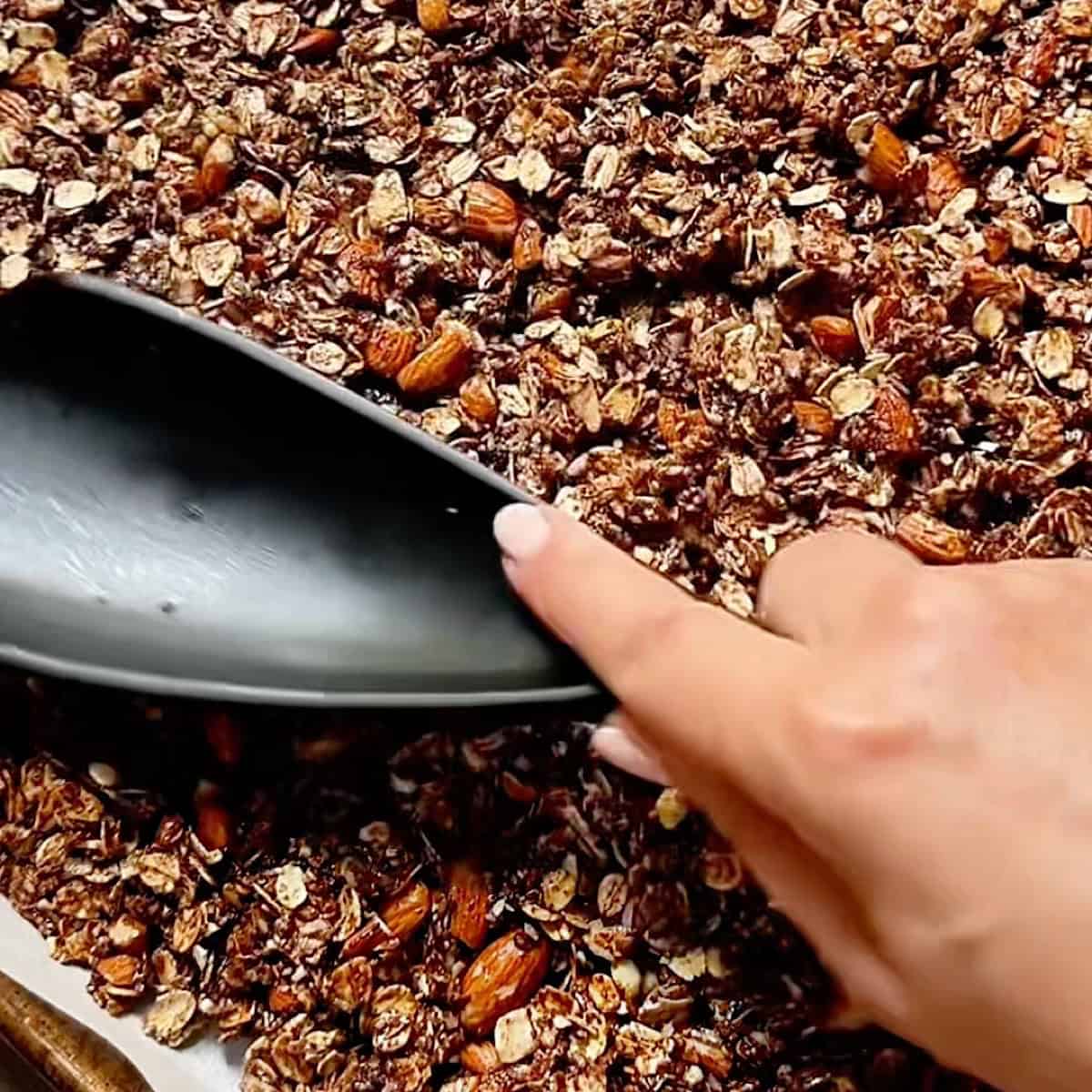 Dark chocolate coated granola being pressed down on parchment.