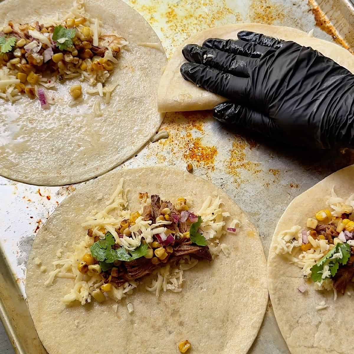 Assembled tacos on a sheet pan and gently pressing one to seal it.