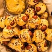 Everything bagel pigs in a blanket and mustard in a plastic basket with parchment.