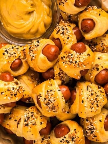 Everything bagel pigs in a blanket and mustard in a plastic basket with parchment.