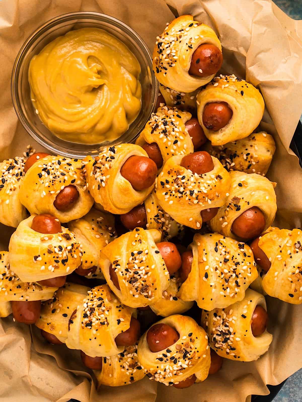 Everything bagel pigs in a blanket and mustard in a plastic basket with parchment.