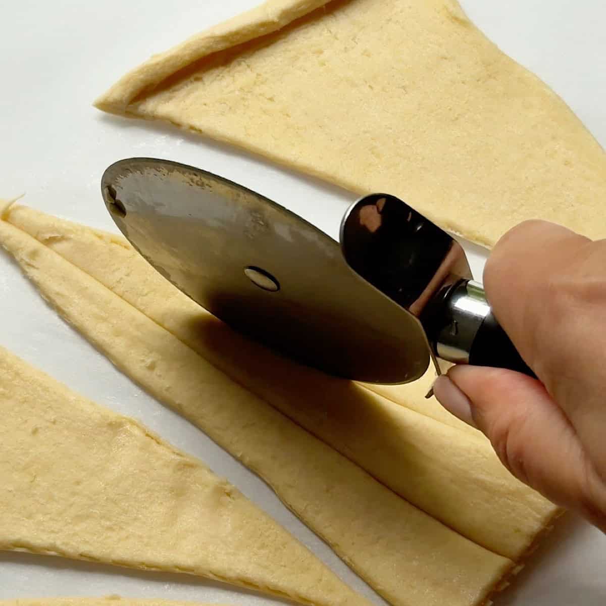 Cutting the refrigerated crescent triangles into three thin strips.