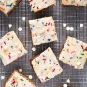 Frosted funfetti blondies on a wire rack with white chocolate chips scattered.