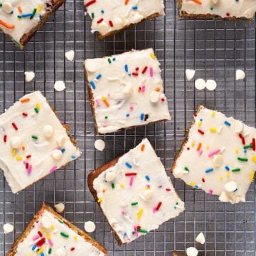 Frosted funfetti blondies on a wire rack with white chocolate chips scattered.