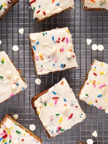 Frosted funfetti blondies on a wire rack with white chocolate chips scattered.