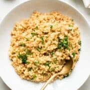 Garlic parmesan couscous with parsley garnish in a white dish with gold spoon.