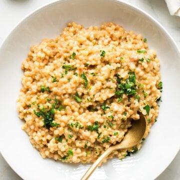 Garlic parmesan couscous with parsley garnish in a white dish with gold spoon.