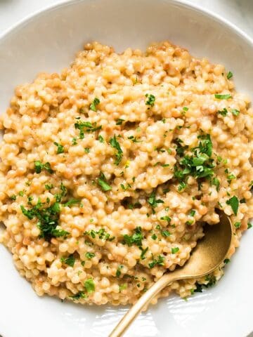 Garlic parmesan couscous with parsley garnish in a white dish with gold spoon.