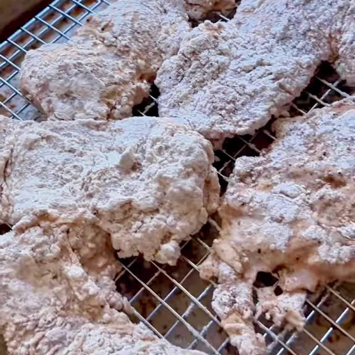 Chicken dredged in flour and seasoning resting on a wire rack to be fried.