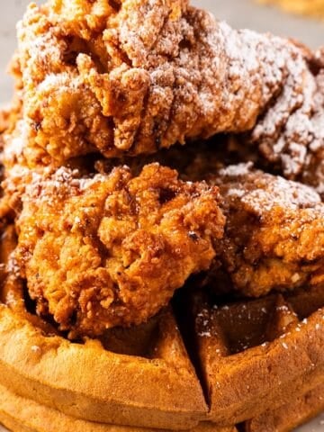 A stack of Belgian waffles with crispy fried chicken, powdered sugar, and spicy maple syrup.