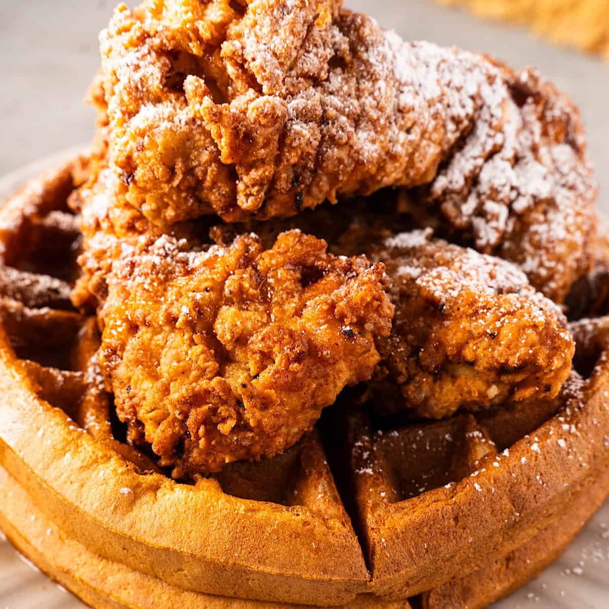 A stack of Belgian waffles with crispy fried chicken, powdered sugar, and spicy maple syrup.