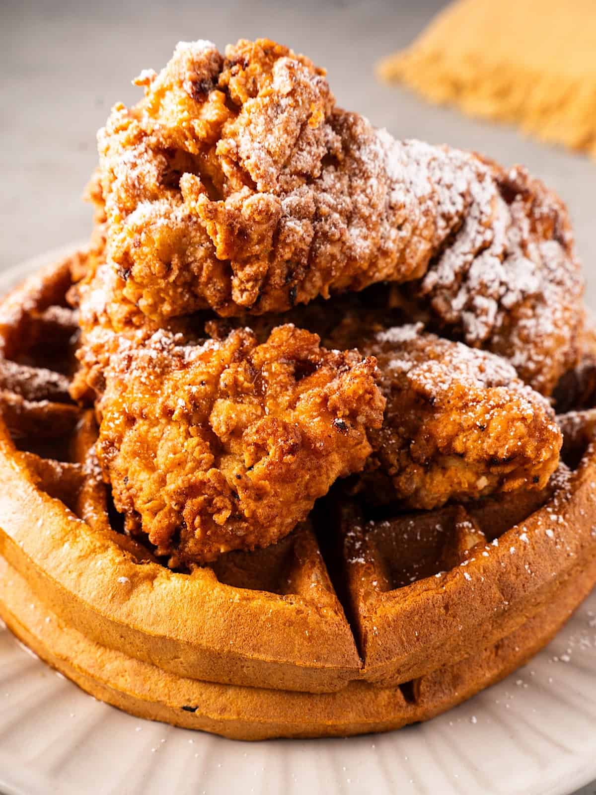 A stack of Belgian waffles with crispy fried chicken, powdered sugar, and spicy maple syrup.