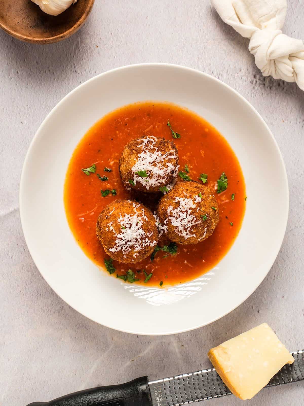 Three garnished arancini plated in a wide shallow bowl with marinara sauce.