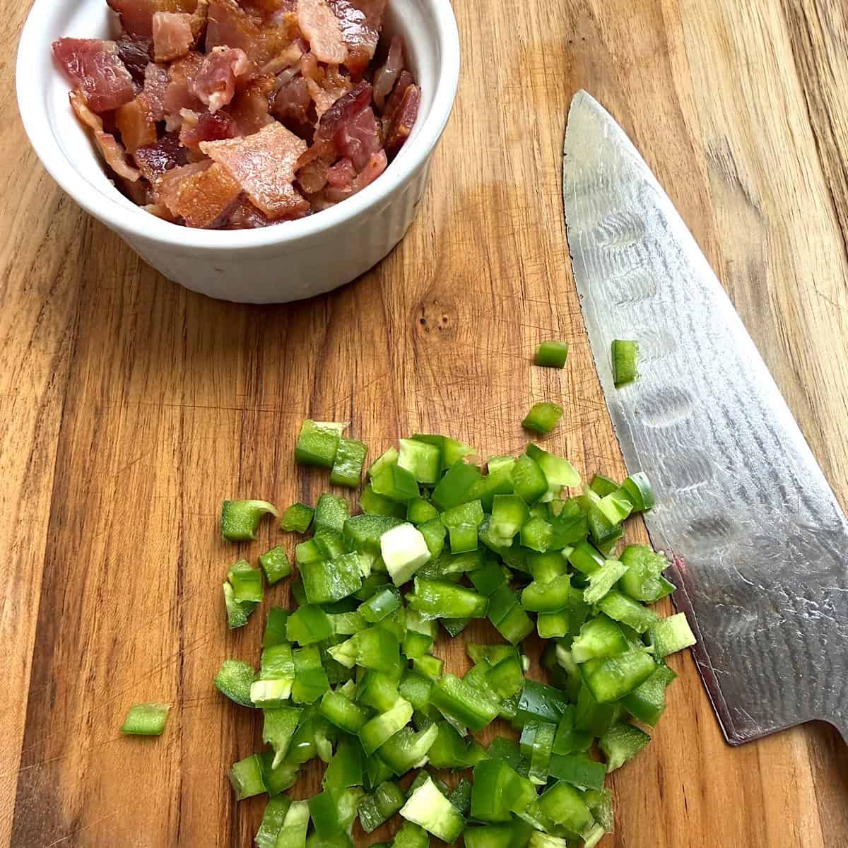 Cooked bacon and jalapeno diced on a cutting board with knife showing.