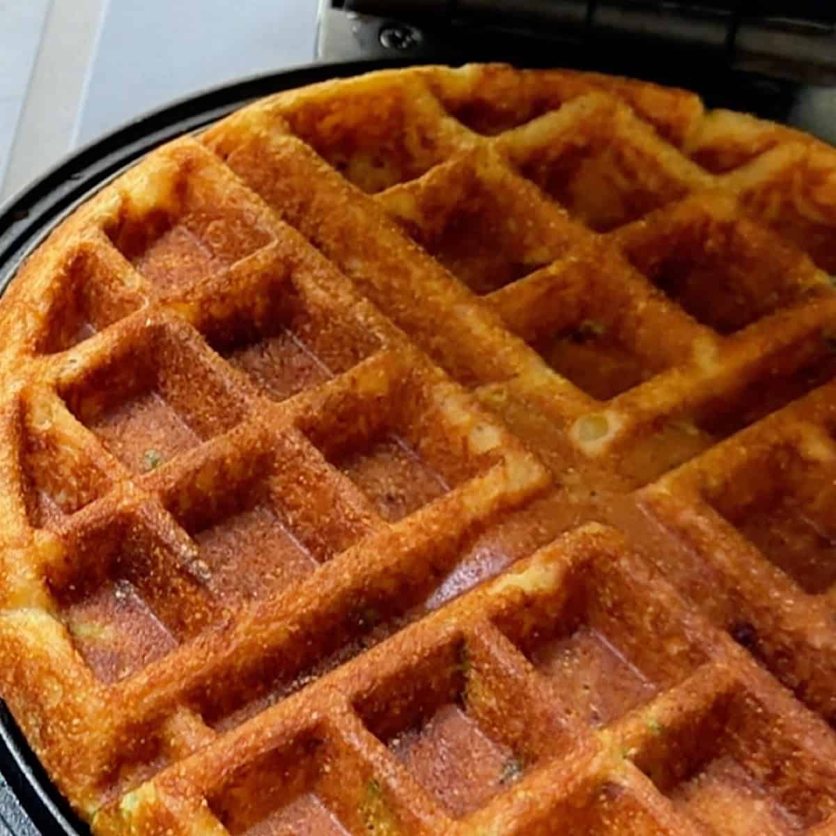 A deeply golden cornmeal waffles in a waffle iron.