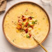 A bowl of bacon potato leek soup with garnish and gold spoon.
