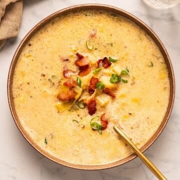 A bowl of bacon potato leek soup with garnish and gold spoon.