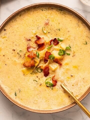 A bowl of bacon potato leek soup with garnish and gold spoon.