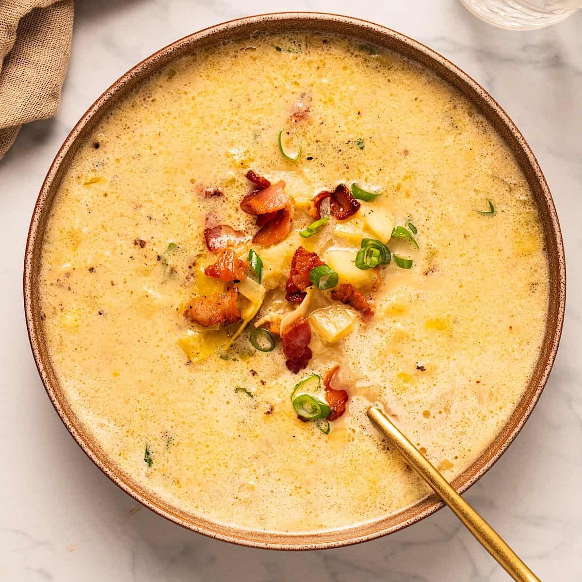 A bowl of bacon potato leek soup with garnish and gold spoon.