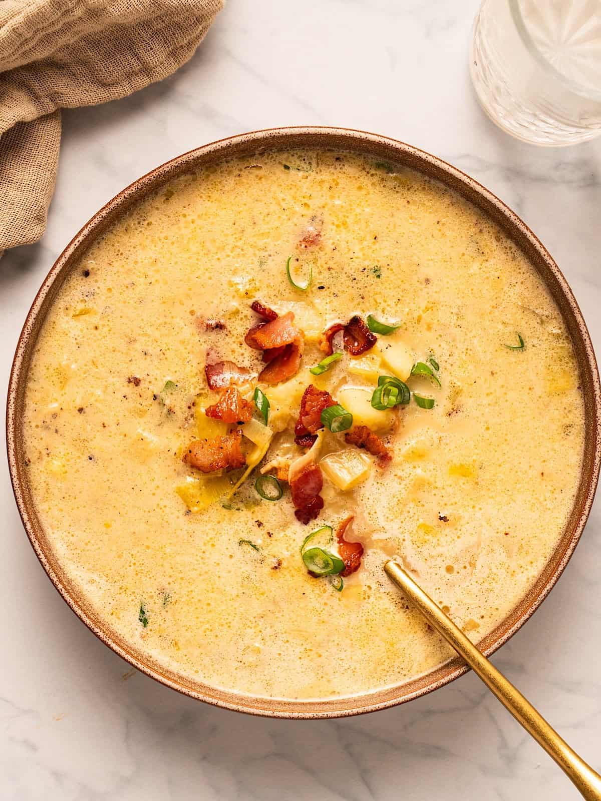 A bowl of bacon potato leek soup with garnish and gold spoon.