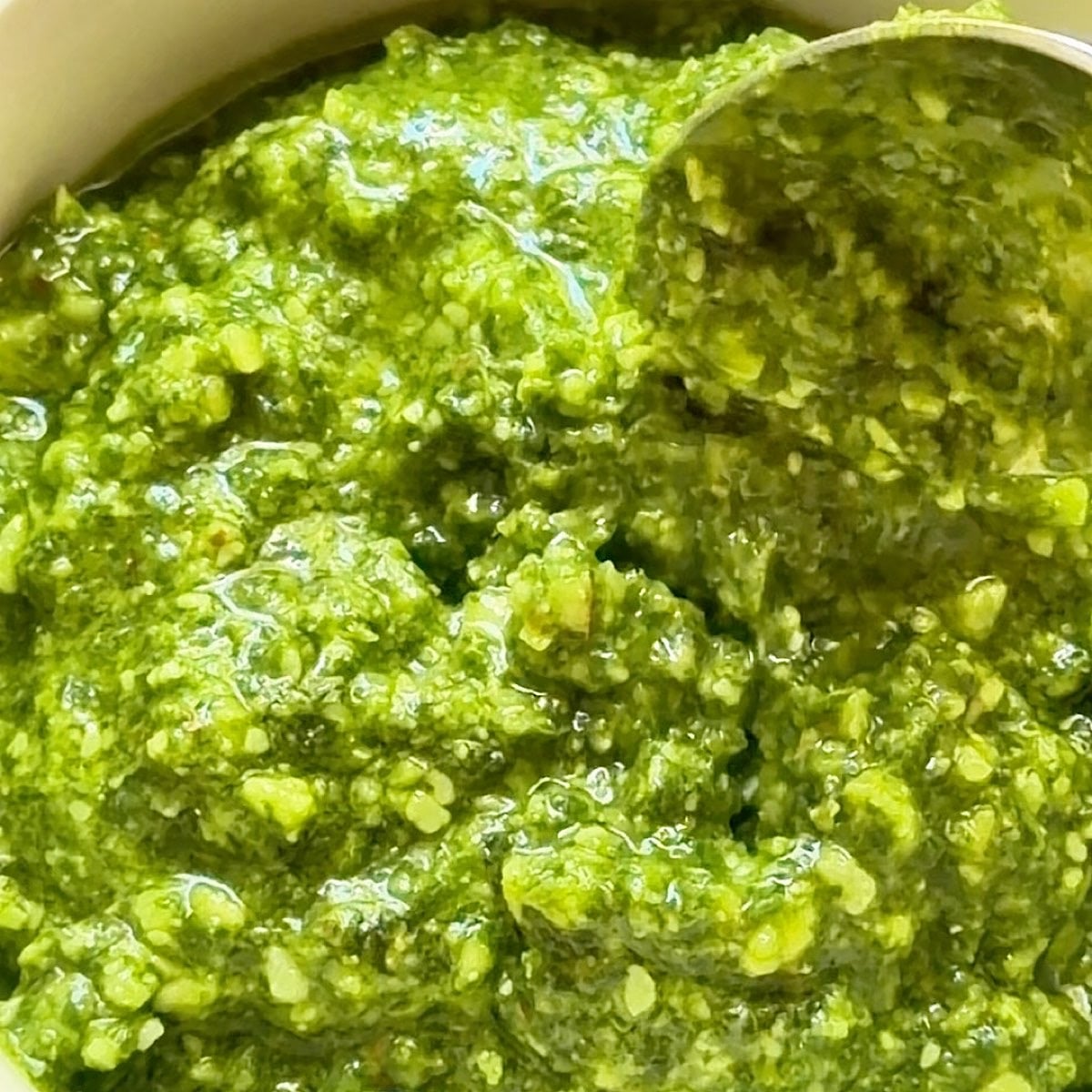 A spoon dipping into the basil pesto with almonds.