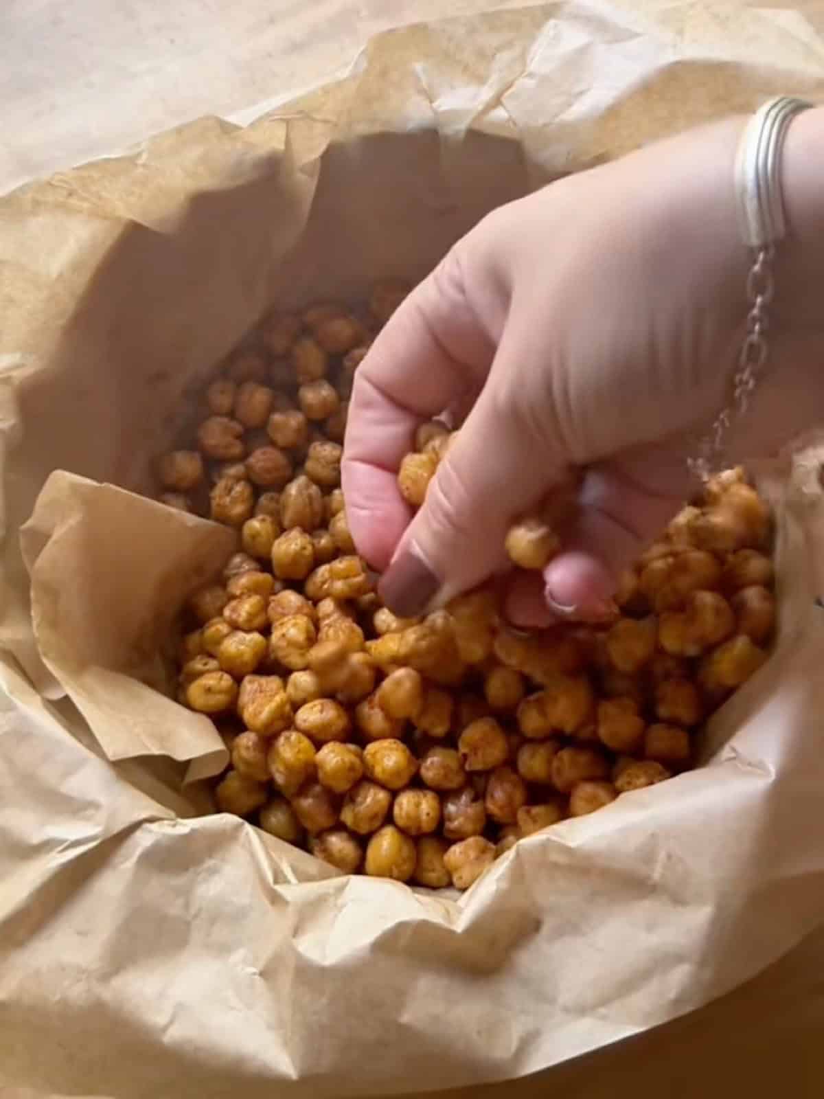 Holding a handful of crispy buffalo chickpeas over a parchment lined bowl.