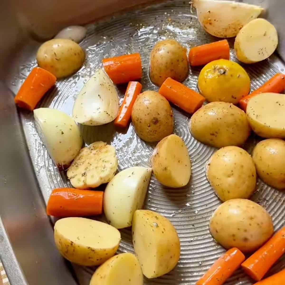 Seasoned vegetables and garlic spread out in roasting pan.