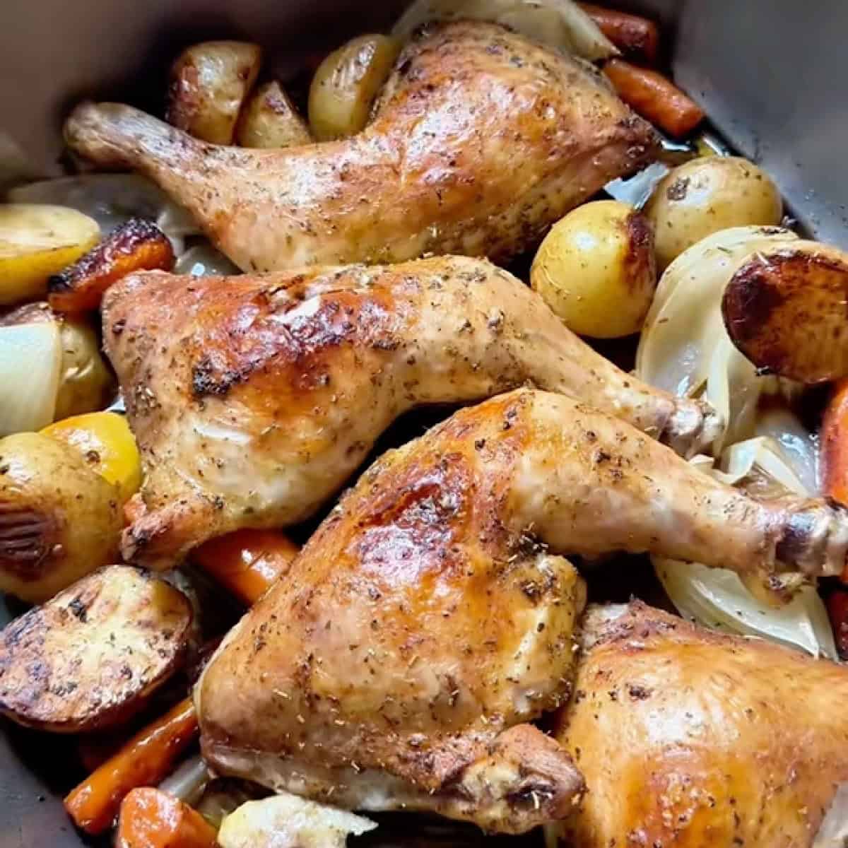 Cooked herb roasted chicken with crispy skin along with vegetables in a roasting pan.