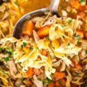 A ladle of turkey noodle soup being held over the slow cooker.