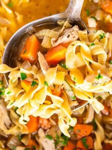 A ladle of turkey noodle soup being held over the slow cooker.