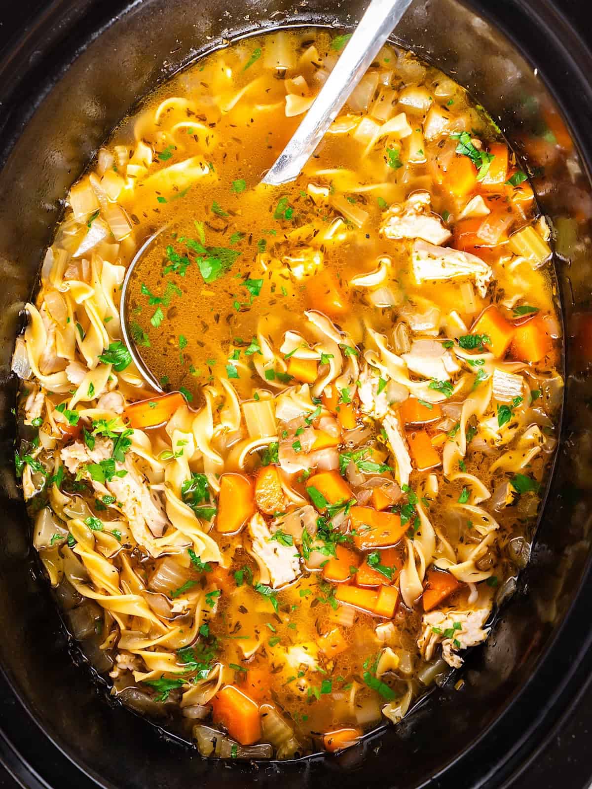 Cooked turkey noodle soup in slow cooker garnished with parsley.