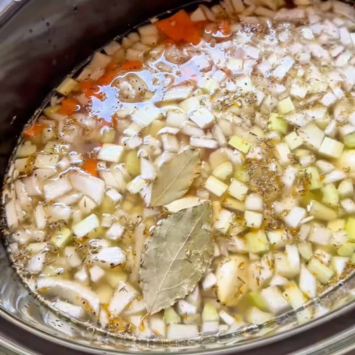 Building the soup with broth, bay leaves, and seasoning.